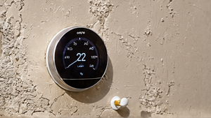 Une main règle le thermostat d’un chauffe-eau dans un local technique domestique.