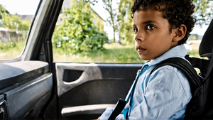 Un parent attache un enfant dans une voiture près d’une école.