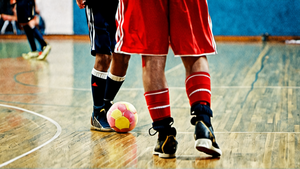 Deux joueurs de futsal disputent un ballon sur un parquet de salle.