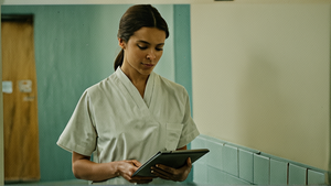 Une soignante consulte une tablette dans un couloir d’hôpital.