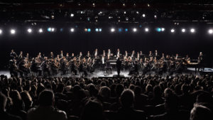 Salle de concert avec orchestre et silhouettes de public, illustrant un concert de musiques de jeux vidéo.