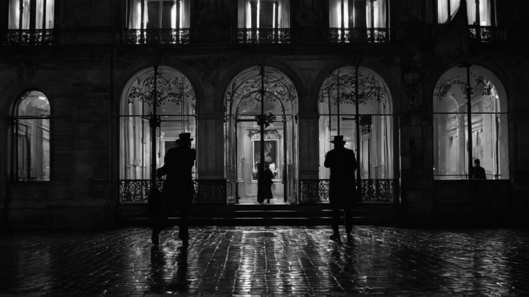 Façade d’un musée éclairée la nuit, avec quelques silhouettes au loin.