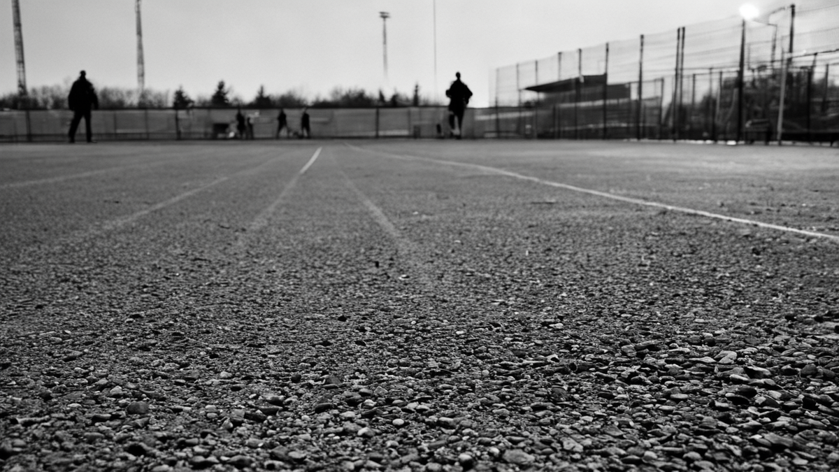 Accès de stade avec barrières de file vides et silhouettes lointaines en fin de journée.