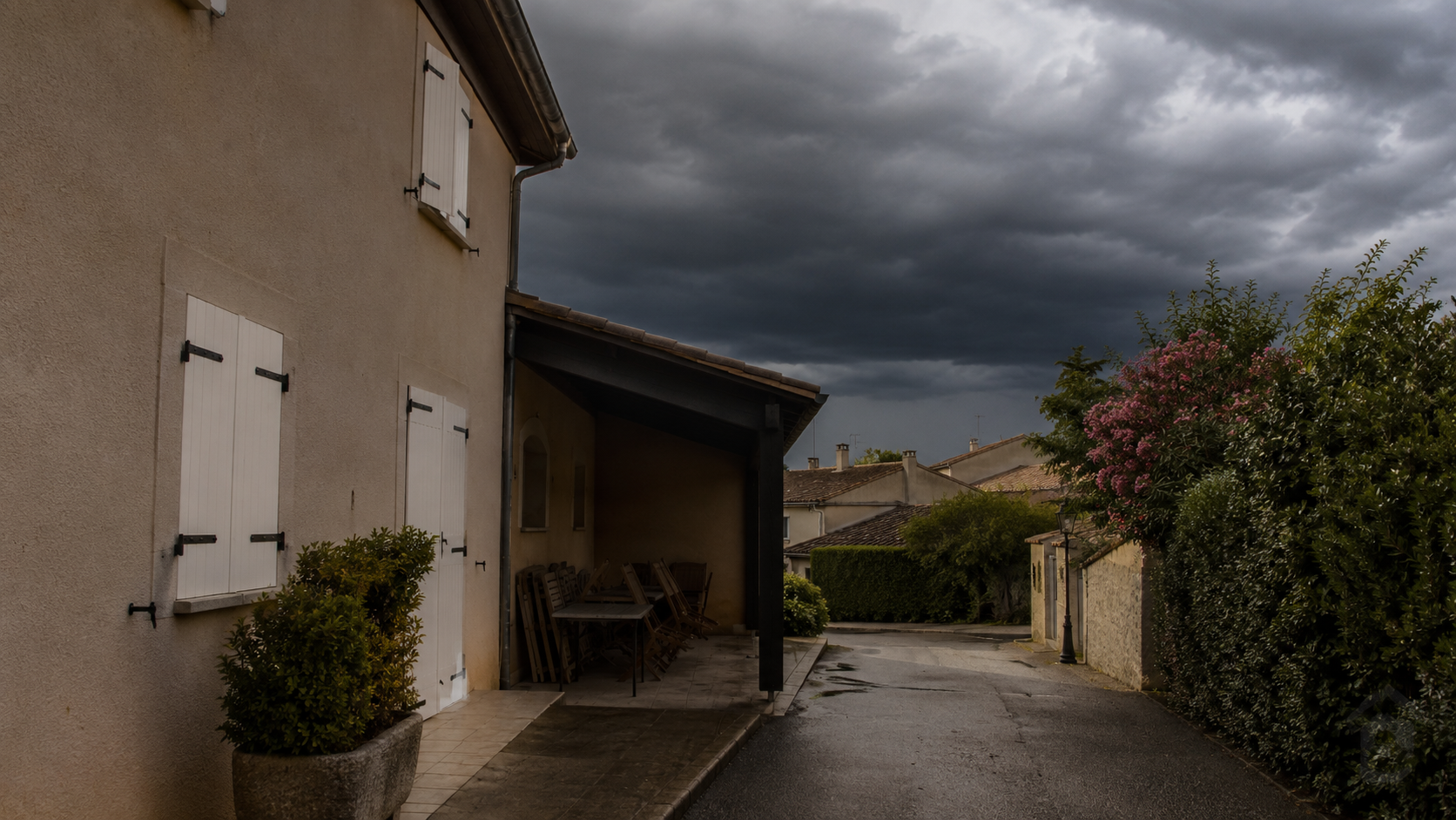 Rue résidentielle préparée avant un orage de chaleur, volets fermés et objets rangés.