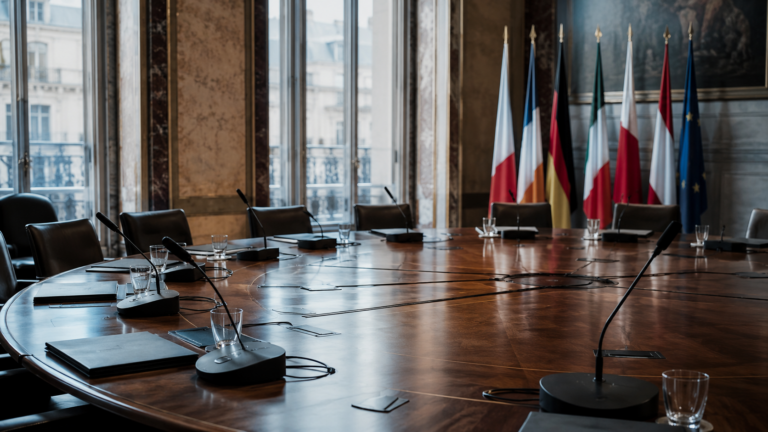 Table de réunion ministérielle vide avec micros et dossiers neutres
