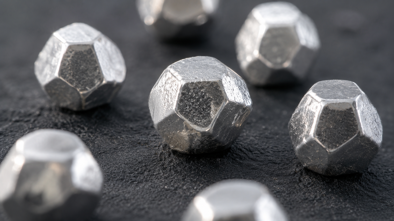De petites formes argentées facettées entre cube et sphère sur une surface sombre.