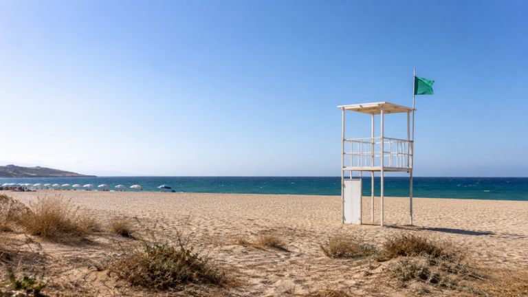 Un poste de secours sur une plage méditerranéenne ensoleillée, drapeau de baignade et mer calme en arrière-plan
