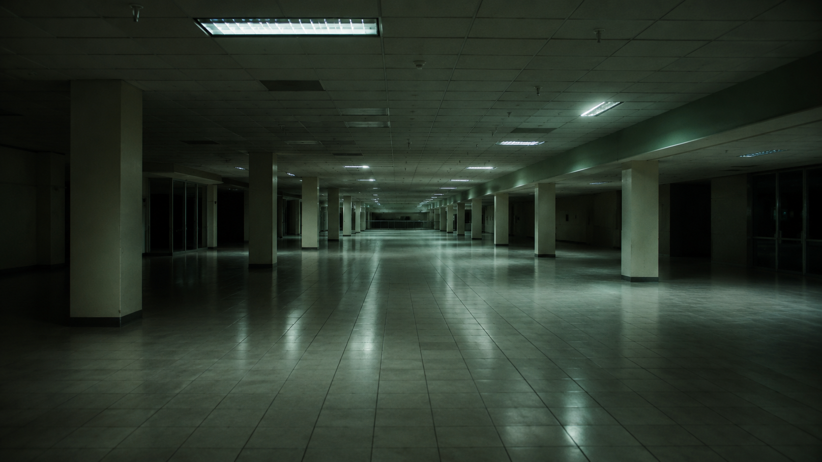 un hall ou un parking désert la nuit, sources lumineuses froides, vide étrange et familier