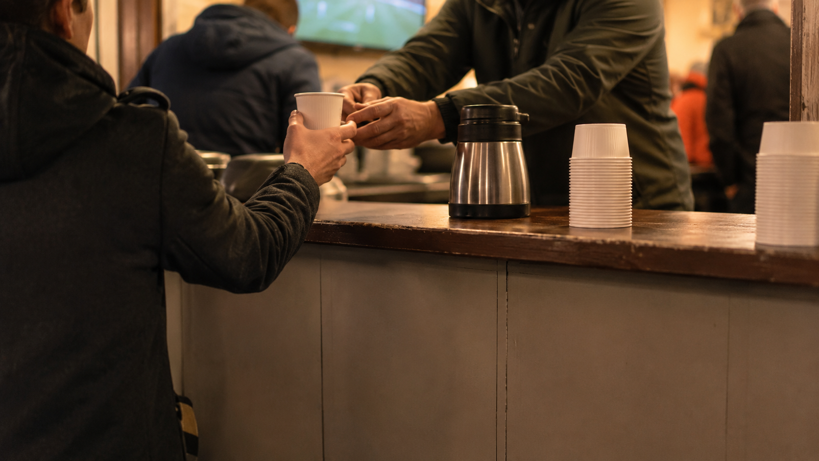 Des bénévoles servent des boissons à la buvette d'un club de foot amateur, vus de dos