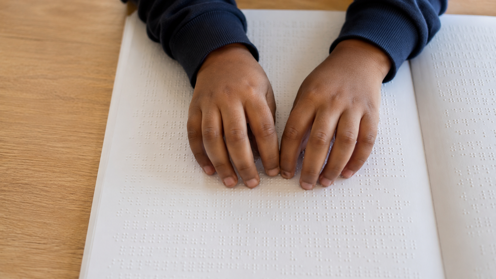 Les mains d'un enfant apprenant à lire un abécédaire en braille sur une table de classe