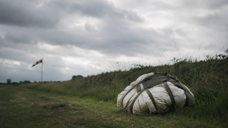 Une piste herbeuse sous ciel gris avec un parachute rond plié au bord du cadre.