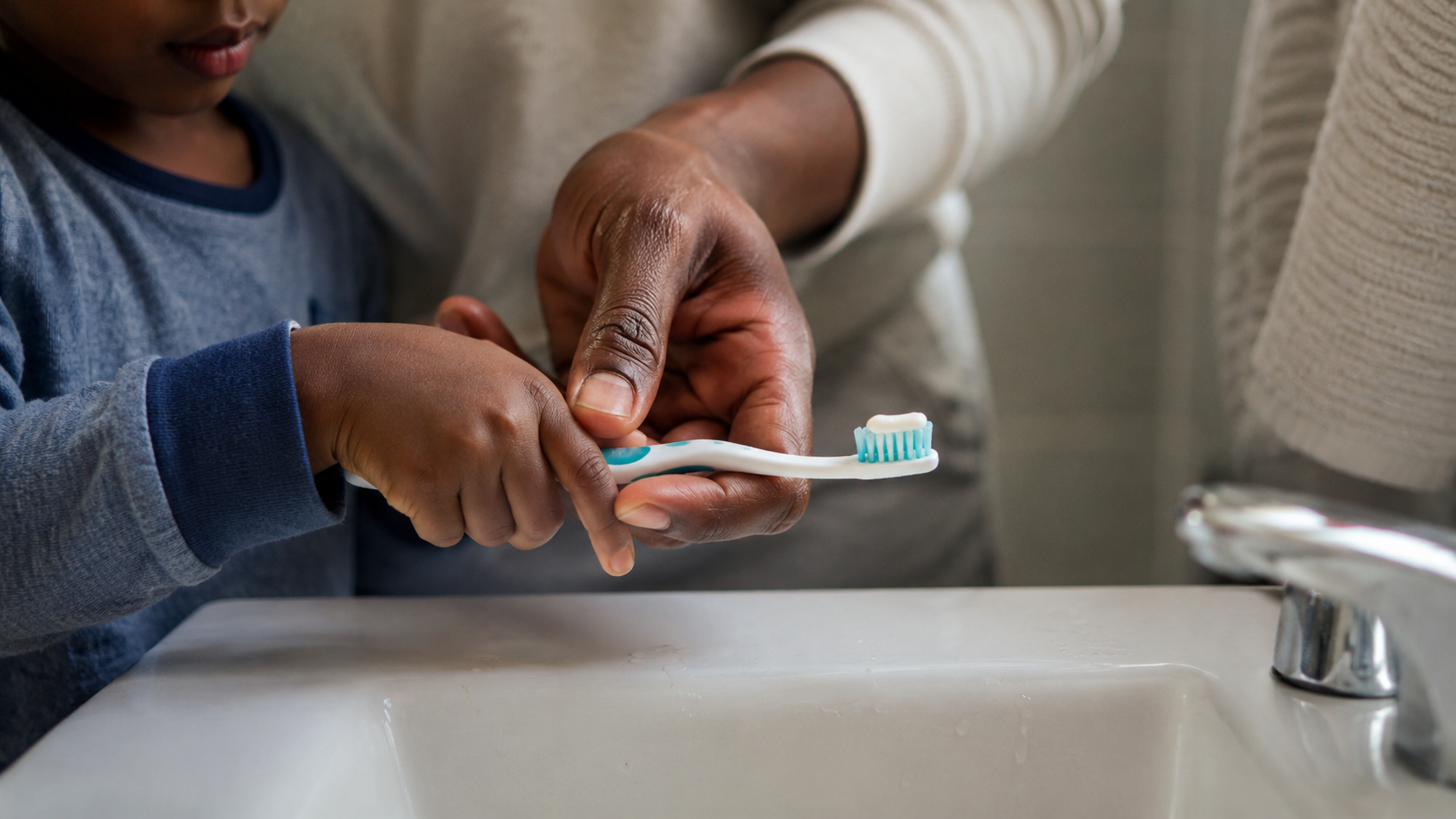 Main d'un enfant tenant une brosse à dents au lavabo, un parent l'aide