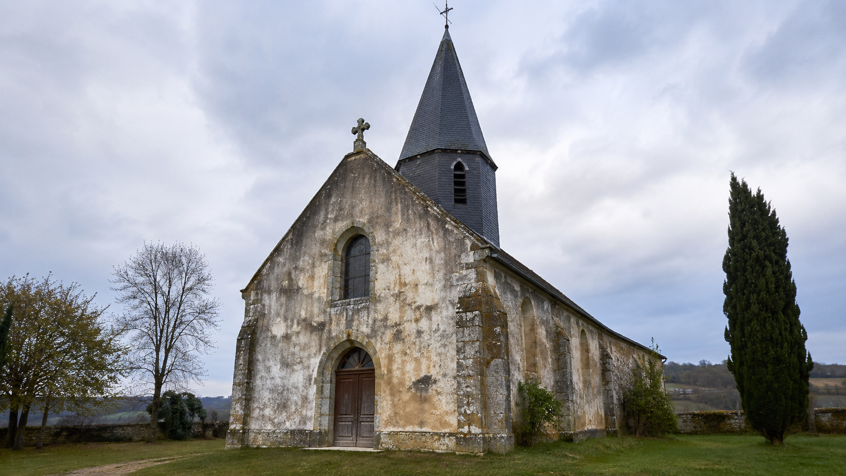 Petite eglise rurale en pierre avec clocher d'ardoise et facade marquee par l'humidite, sur une hauteur de village