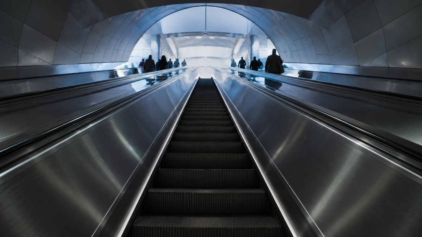 Un long escalator de métro avec des voyageurs immobiles en silhouette des deux côtés