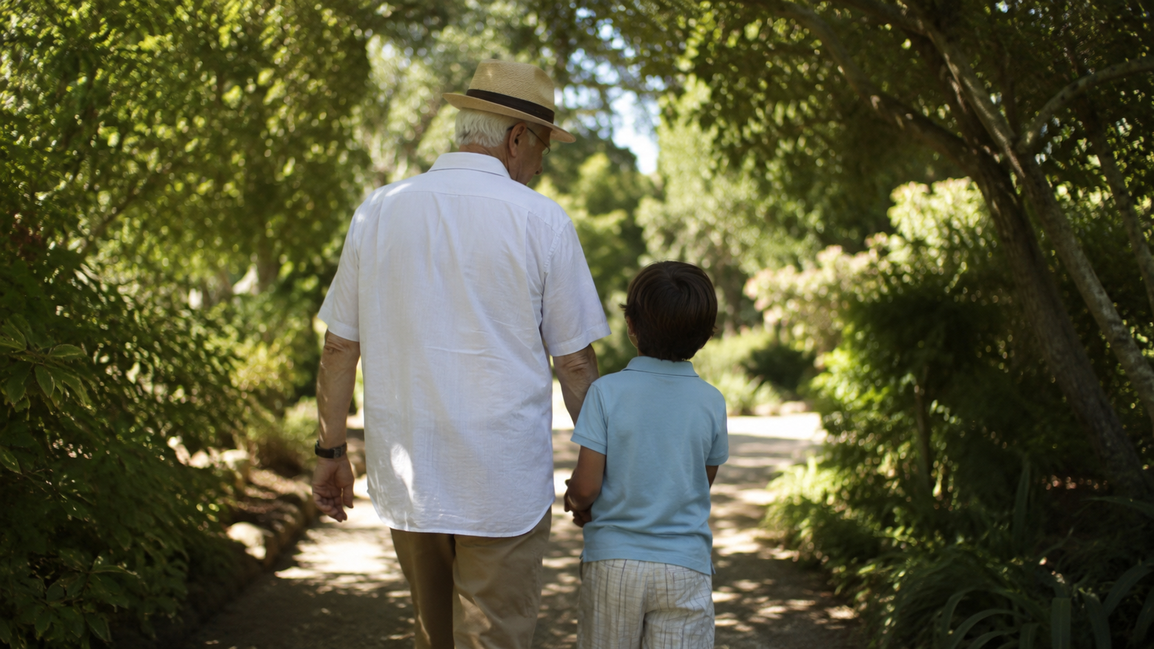 Un grand-parent et un jeune enfant vus de dos marchent dans un jardin ombragé un après-midi d'été