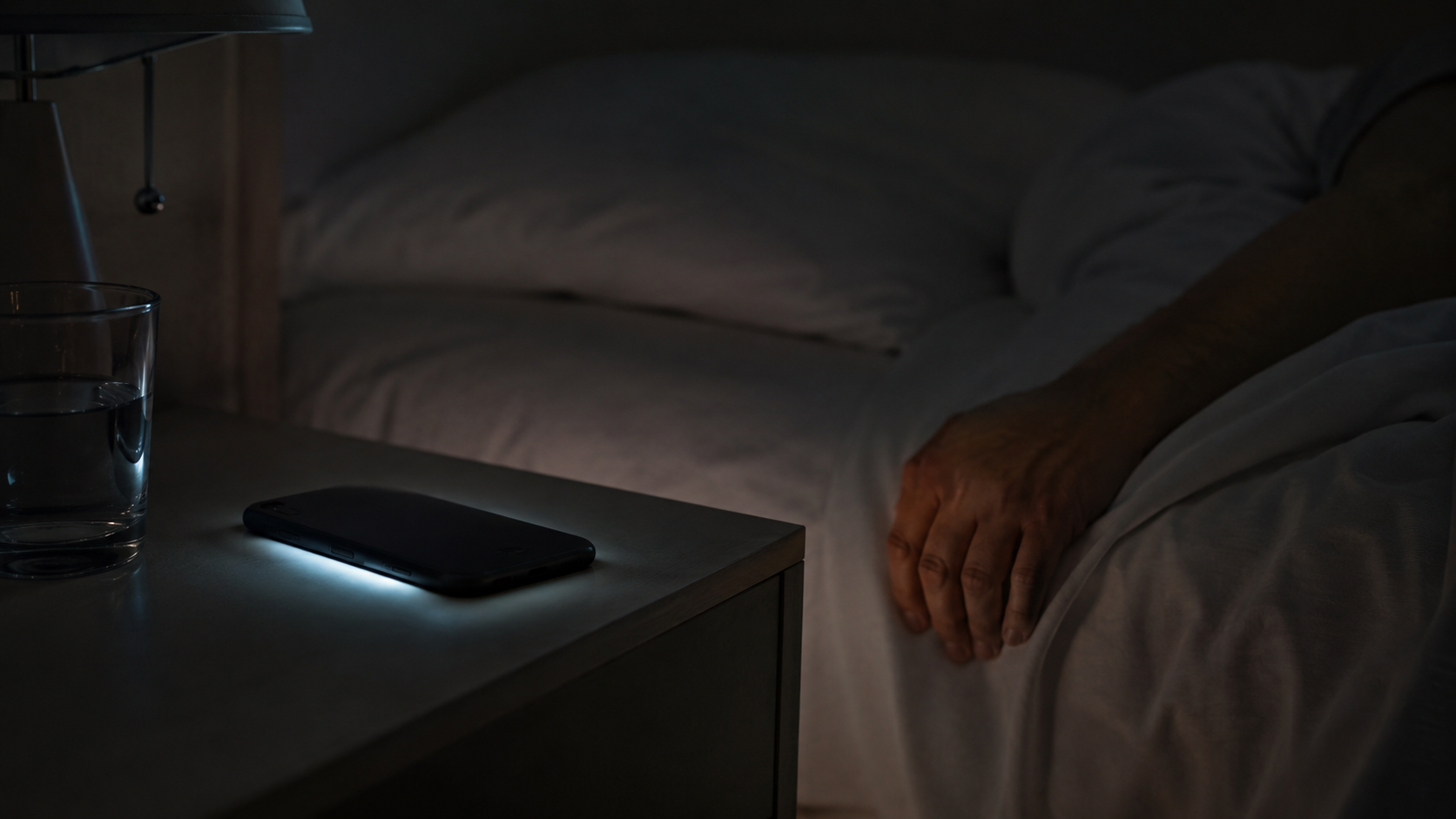 Smartphone retourne sur une table de nuit, lueur d'ecran dans une chambre sombre