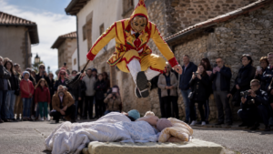 Personnage costumé en jaune et rouge bondissant au-dessus de matelas dans une ruelle de village espagnol pendant la fête El Colacho