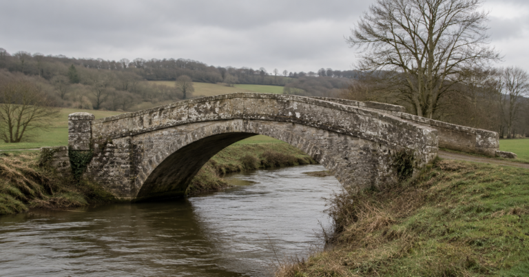un petit pont de pierre de campagne française, fissures et béton patiné, enjambant une rivière étroite, sous un ciel couvert