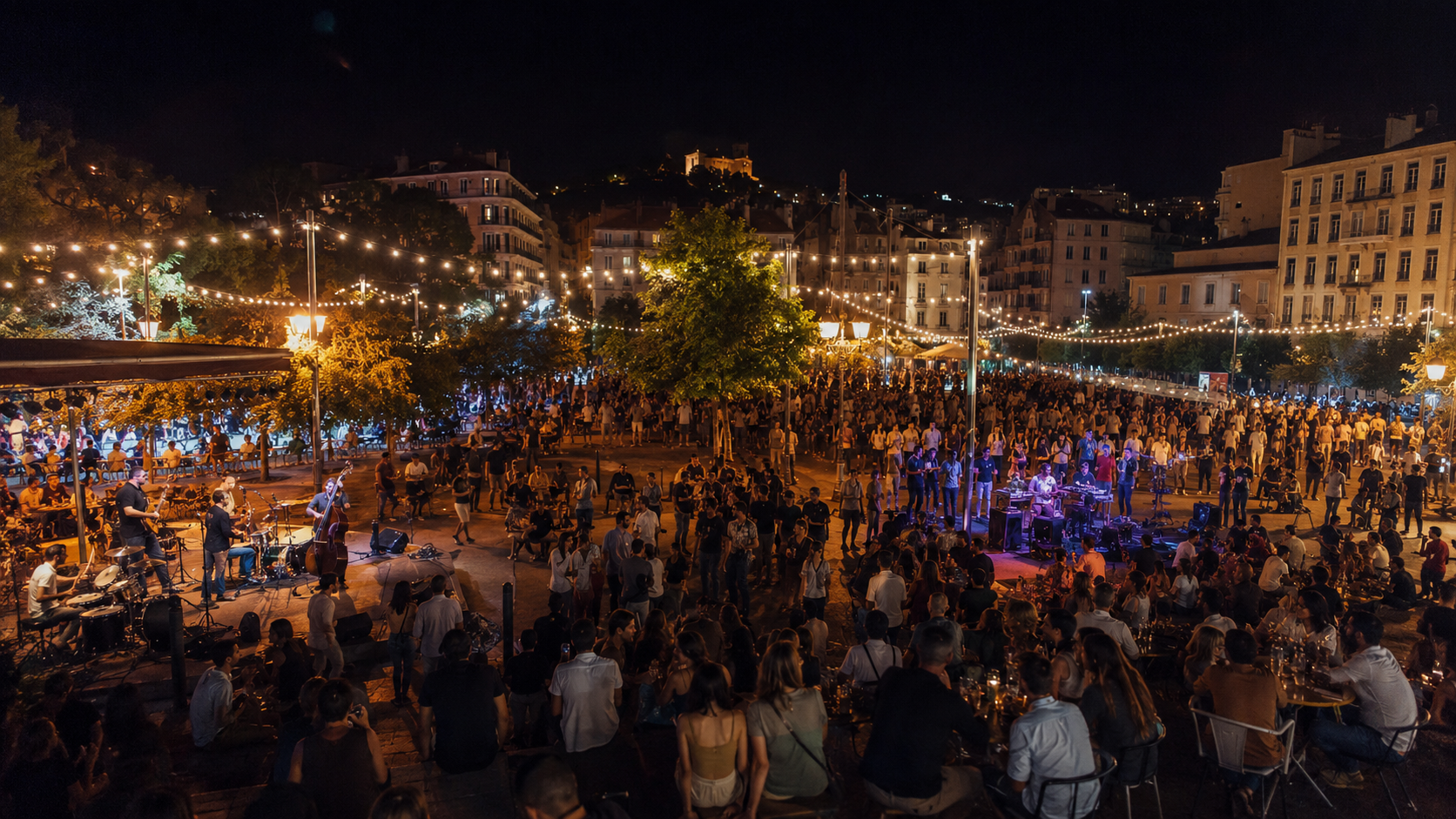 Une place de ville animée la nuit pendant la fête, plusieurs scènes et une foule sous des guirlandes lumineuses