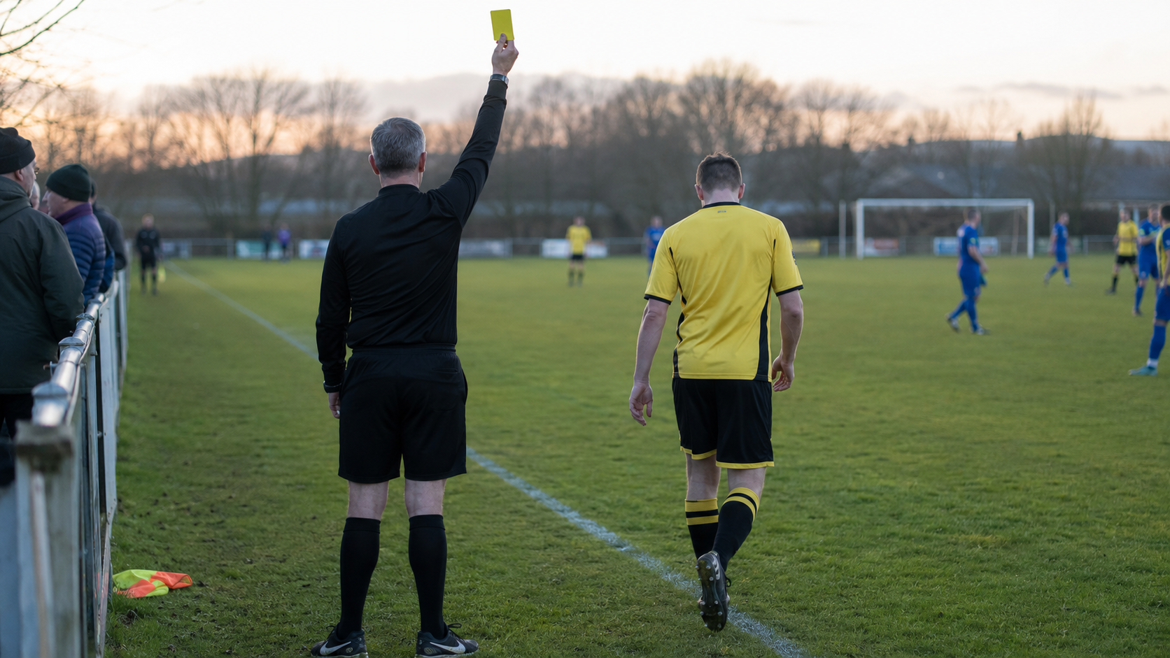 Arbitre amateur brandissant un carton tandis qu'un joueur regagne la touche