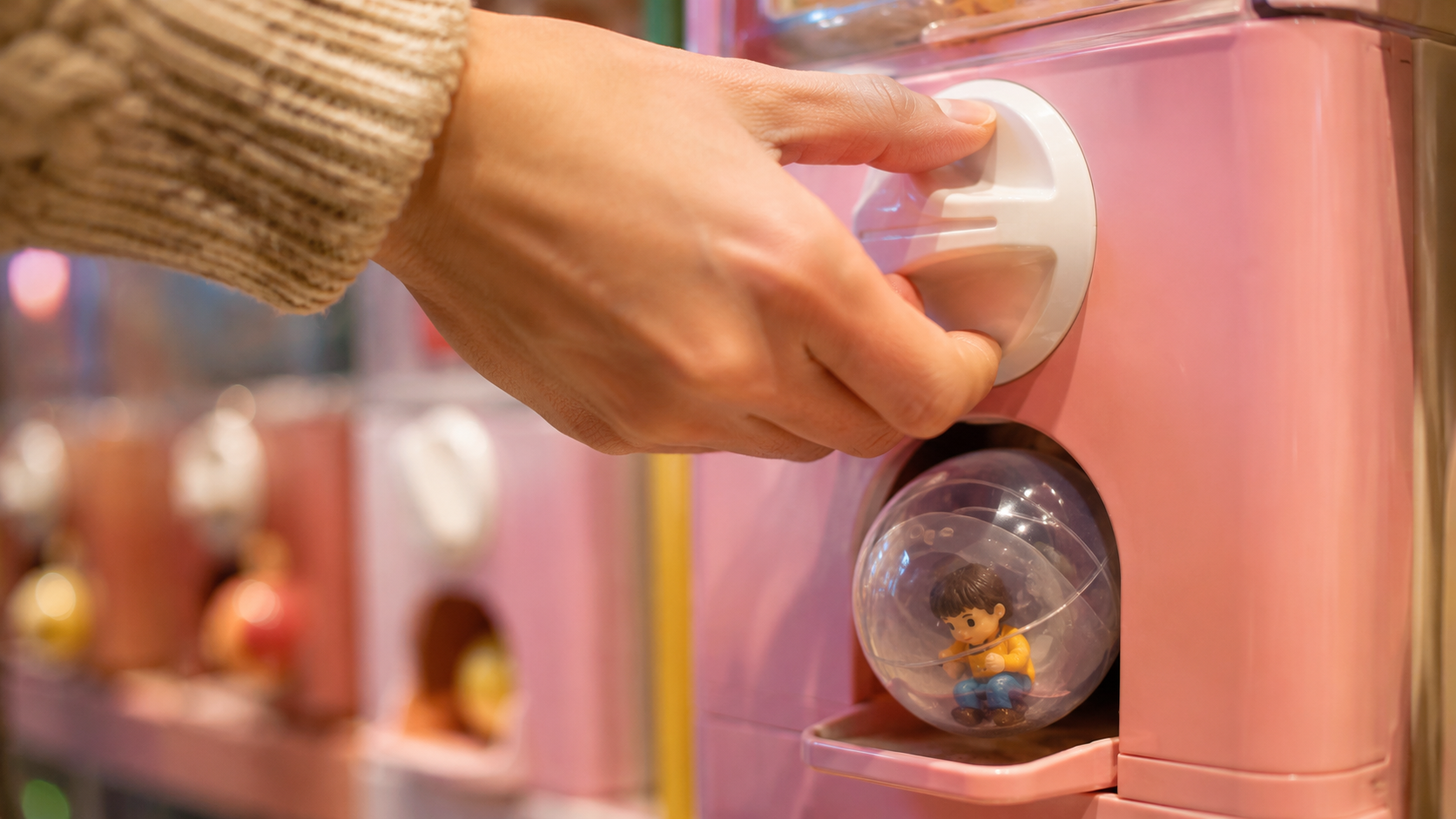 Gros plan sur une main qui tourne la mollette d'une machine a capsules, une boule transparente tombe dans le bac