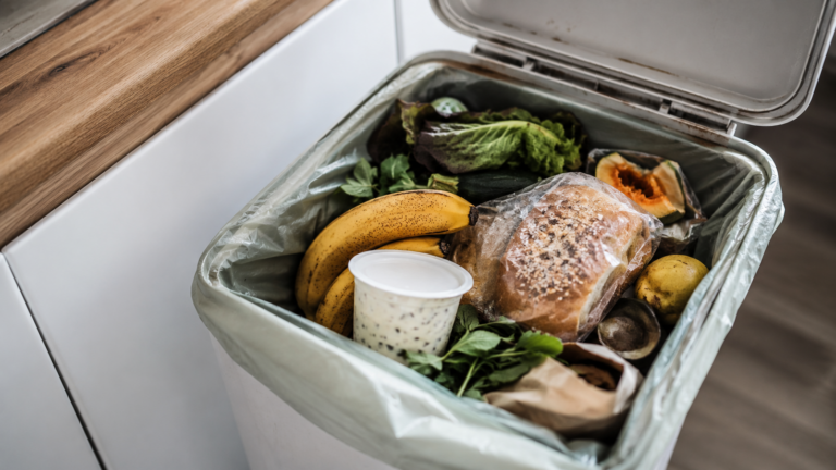Une poubelle de cuisine ouverte contenant des aliments encore emballés et consommables