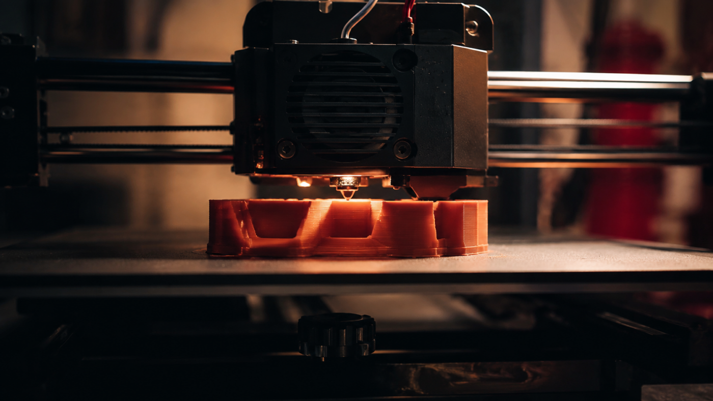 Une imprimante 3D de bureau fabrique une pièce plastique dans un atelier maison faiblement éclairé