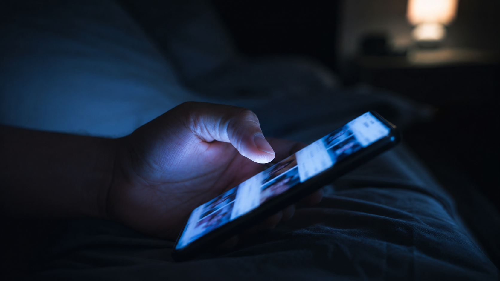 Main faisant défiler un smartphone dans la pénombre, lueur bleutée de l'écran