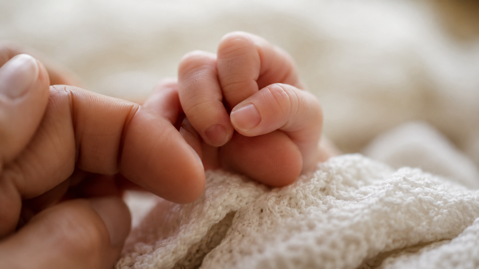 La petite main d'un nouveau-né refermée autour d'un doigt d'adulte sur une couverture claire