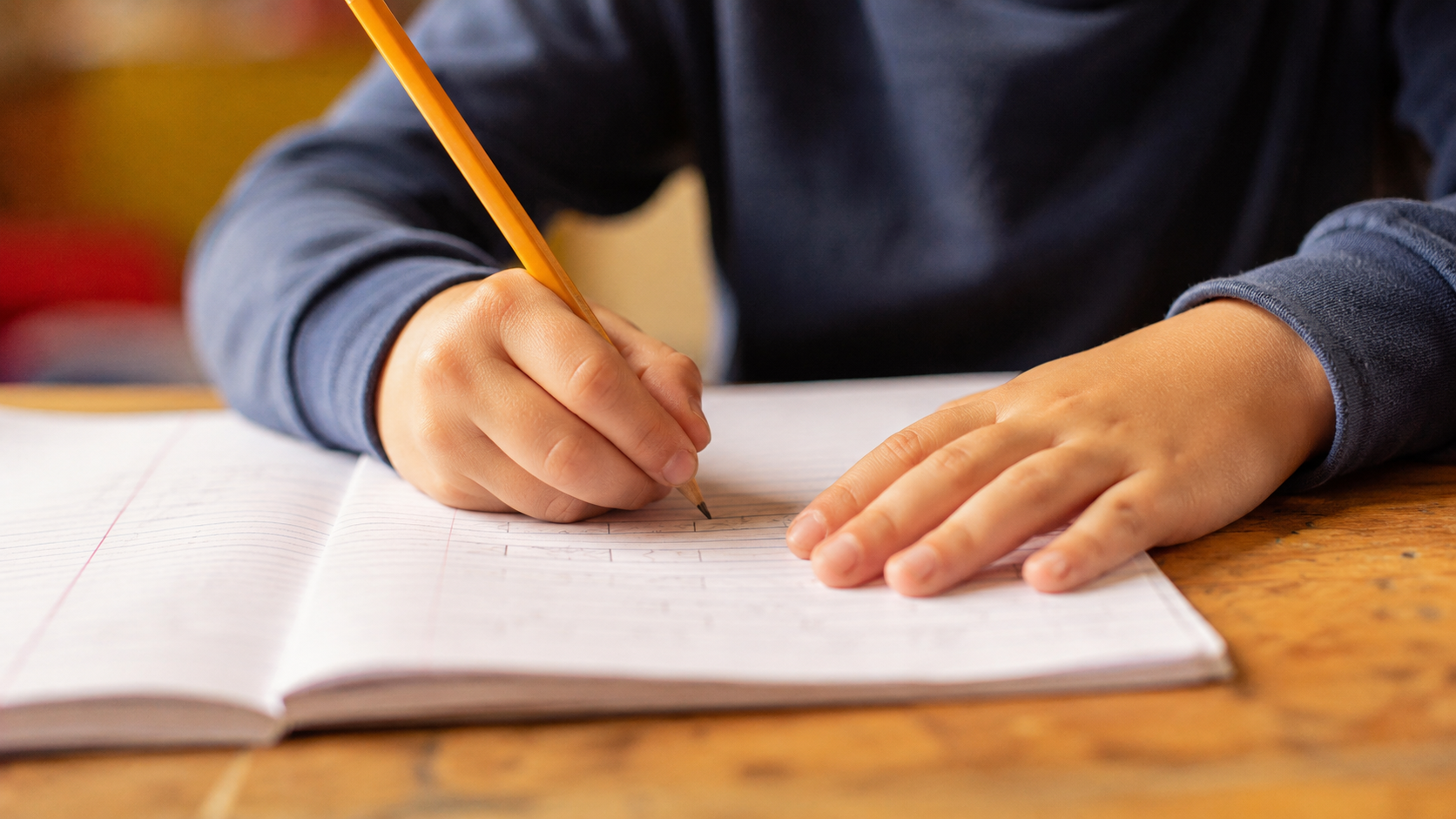 Les mains d'un enfant qui écrit au crayon dans un cahier papier sur un pupitre d'école