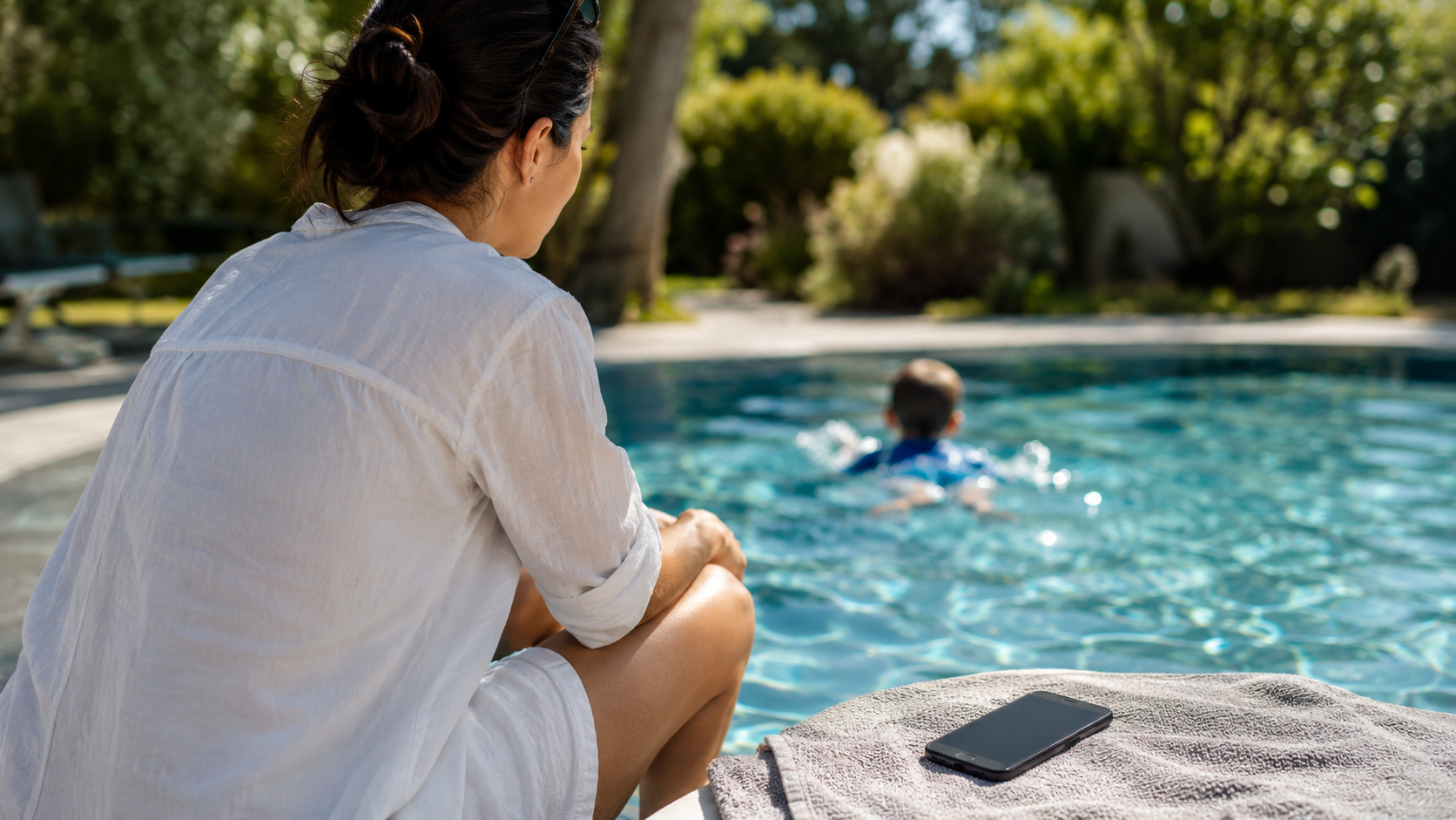 Un adulte surveille attentivement l'eau d'un bassin, téléphone posé à l'écart