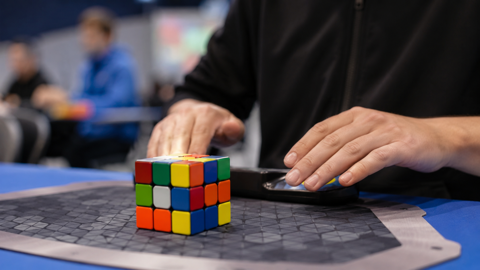 Mains d'un compétiteur de speedcubing au-dessus d'un tapis de chronométrage avec un casse-tête coloré