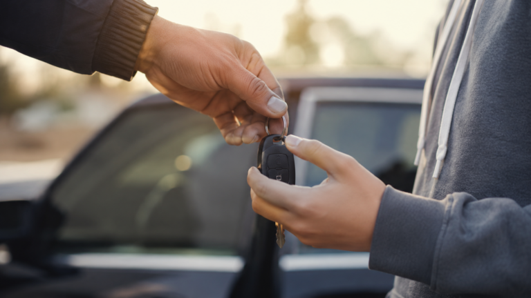 Une main d'adulte tend un trousseau de clés de voiture à un adolescent près d'une porte d'entrée