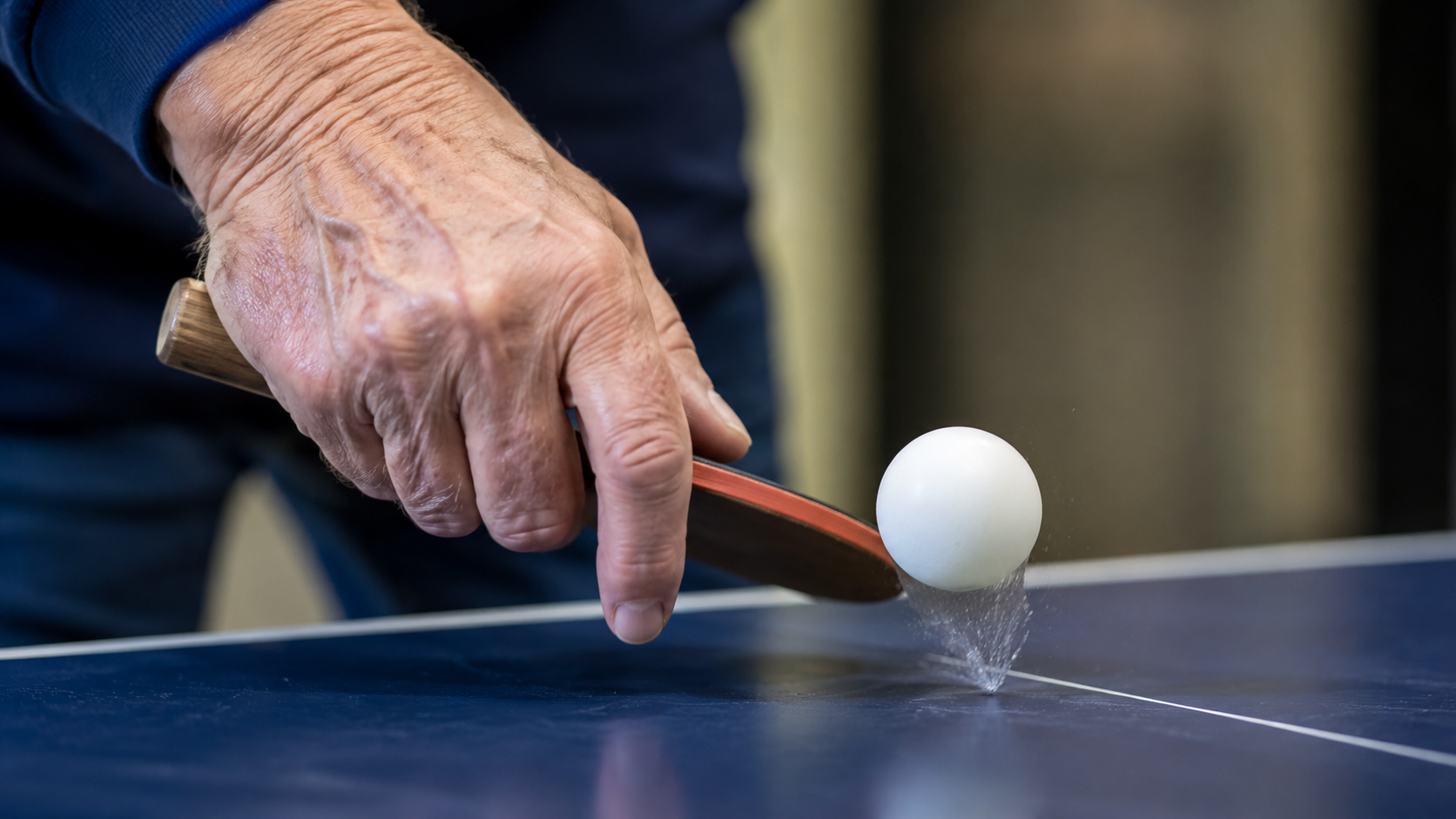 gros plan sur une main âgée et une balle de ping-pong en plein rebond sur la table
