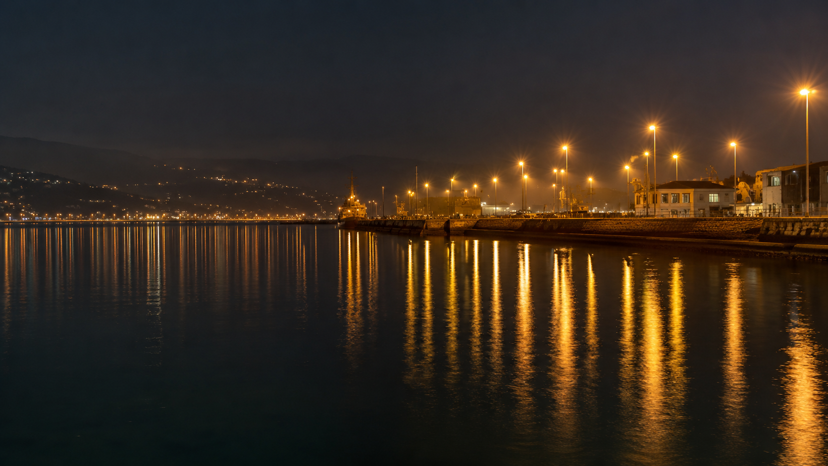 Lumières d'un port et d'une route côtière se reflétant sur une mer sombre la nuit