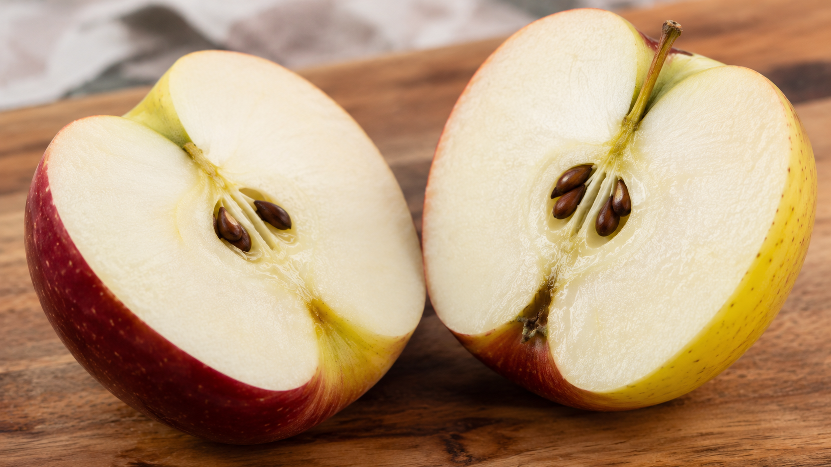 Une pomme coupée en deux sur une planche en bois, chair et pépins apparents