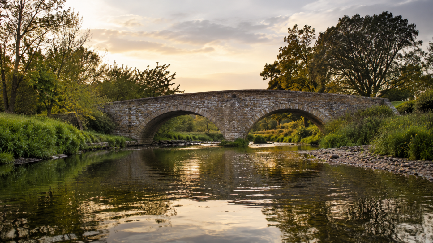 Petit pont de pierre au-dessus d'une riviere de campagne au crepuscule, eau calme et berges vertes