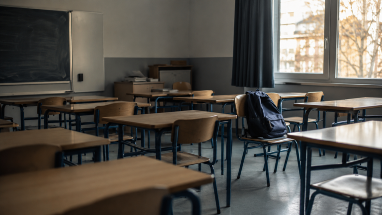 Salle de classe de lycée vide en fin de journée, un sac d'élève posé sur une chaise près de la fenêtre