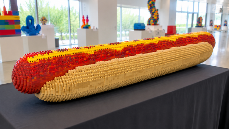 Une longue sculpture en briques colorees en forme de saucisse dans un pain, exposee sur une table