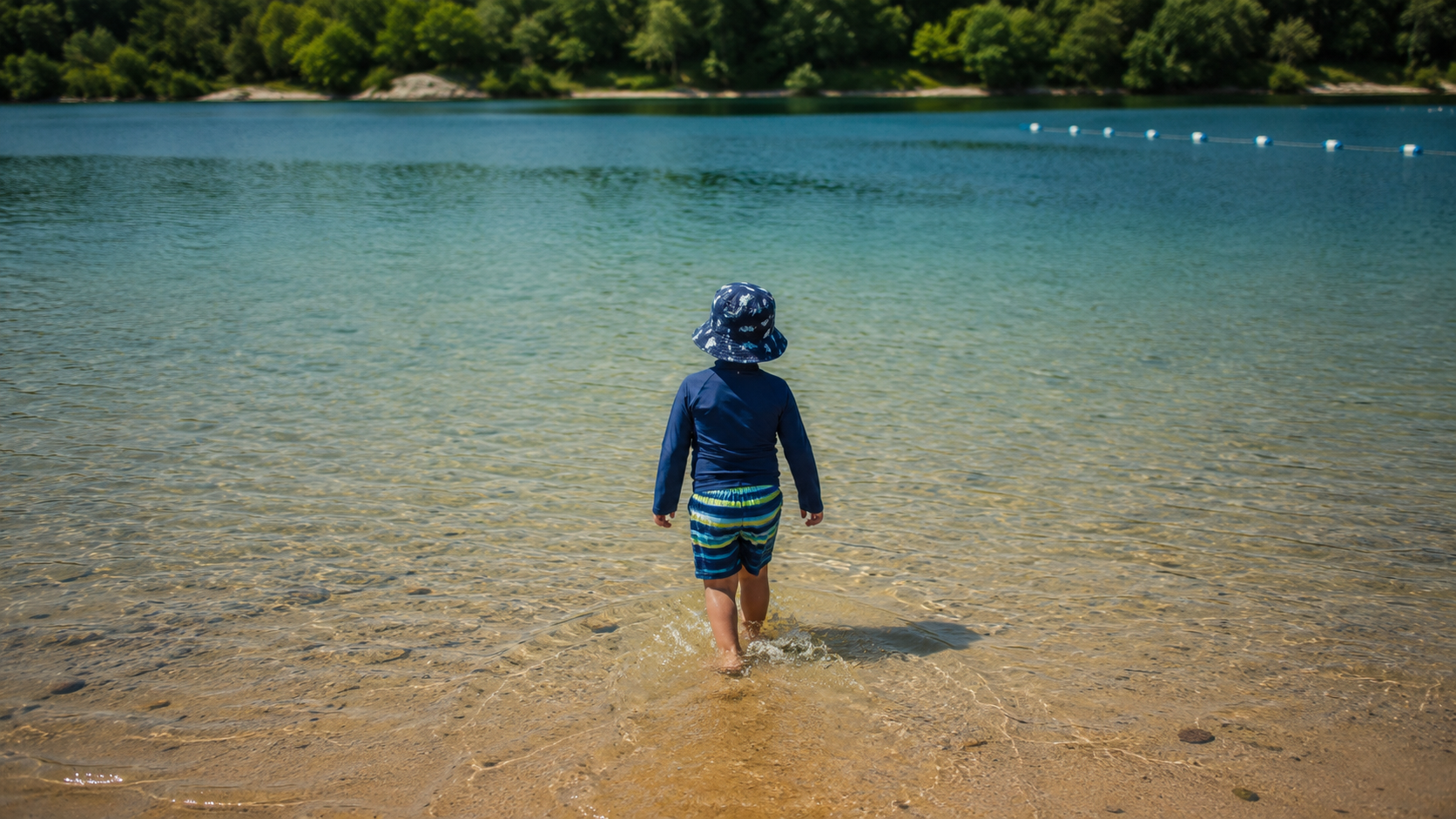 Un enfant vu de dos entrant dans l'eau peu profonde d'un plan d'eau l'ete