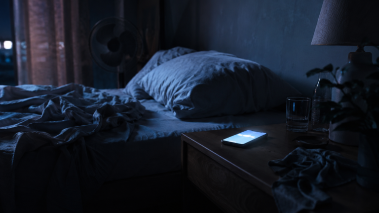 Une chambre la nuit avec un smartphone allume sur la table de chevet pres d'un lit froisse