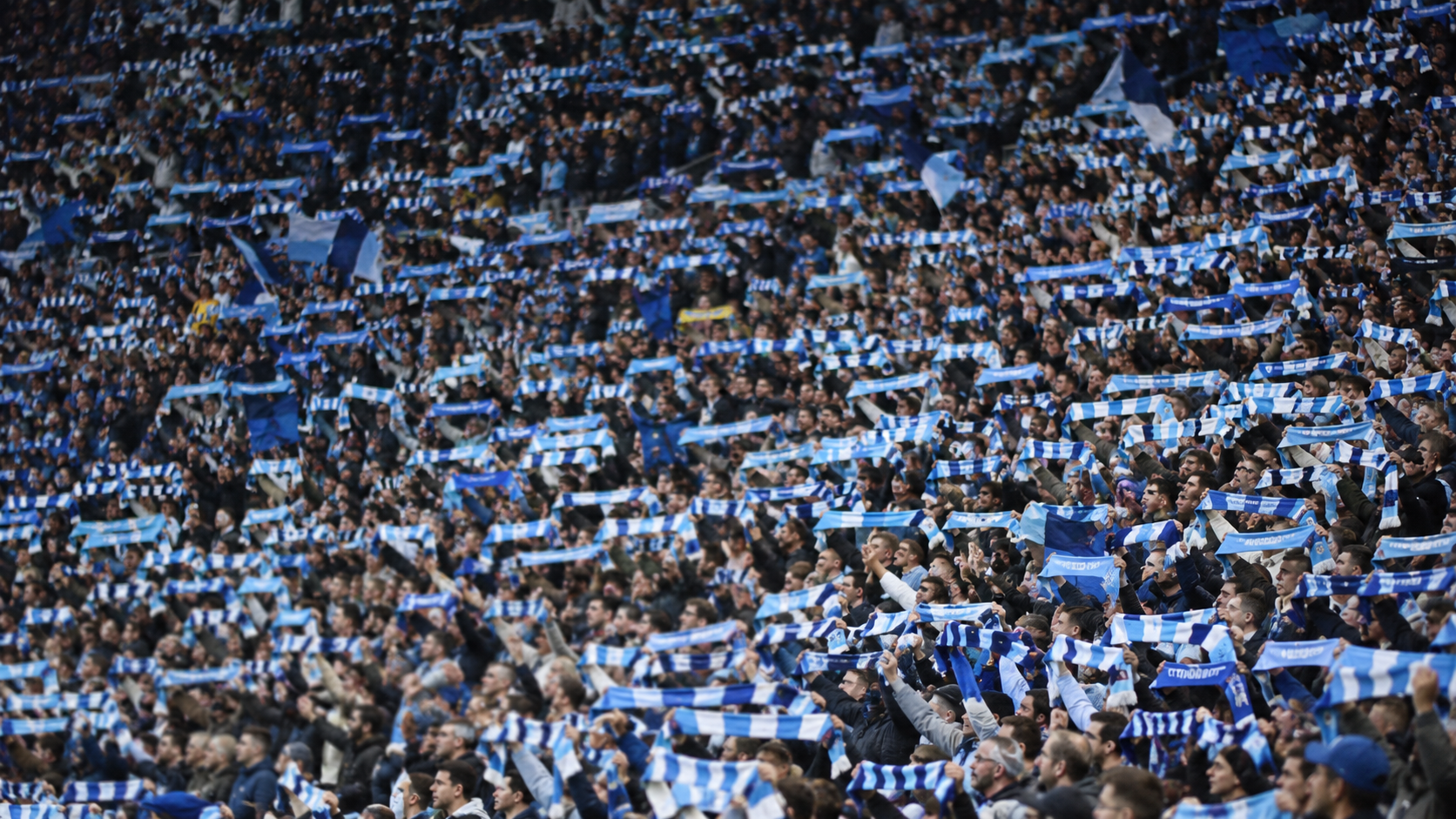 Des tribunes de stade remplies de supporters agitant des écharpes, en vue large
