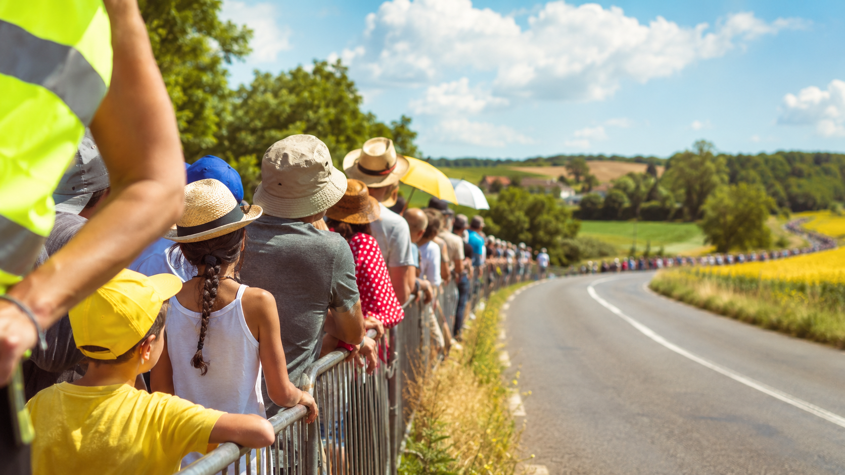 Spectateurs au bord d'une route de campagne attendant une course cycliste, chasuble de bénévole au premier plan
