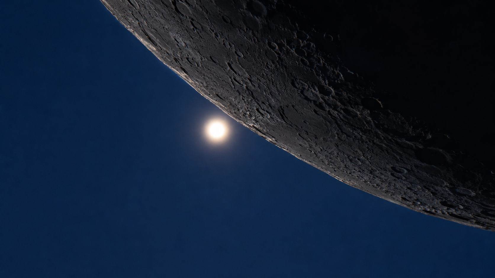 Le bord sombre de la Lune près d’un point lumineux dans un ciel bleu.