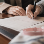Mains d'adultes remplissant un formulaire d'état civil avec un stylo sur un bureau, un bracelet de maternité posé à côté