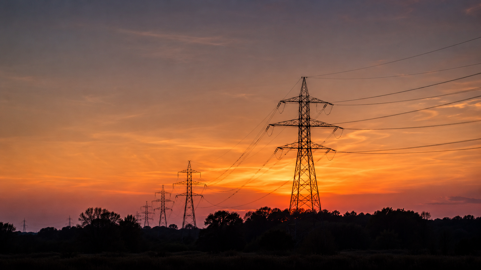 Ligne à haute tension et pylônes se détachant sur un ciel de crépuscule orange