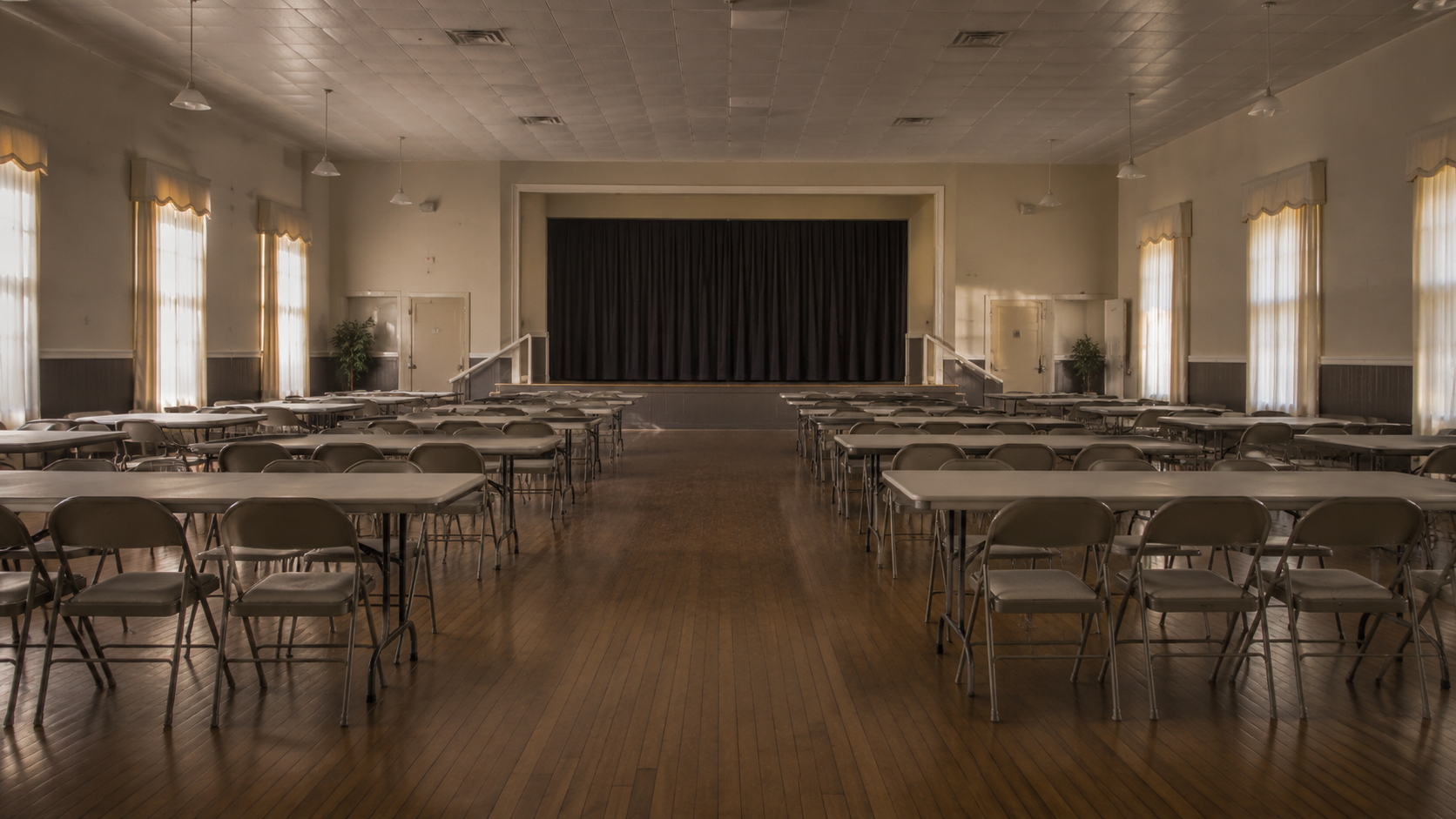 Salle des fêtes associative avec des chaises pliantes alignées et des tables vides, sans personne.