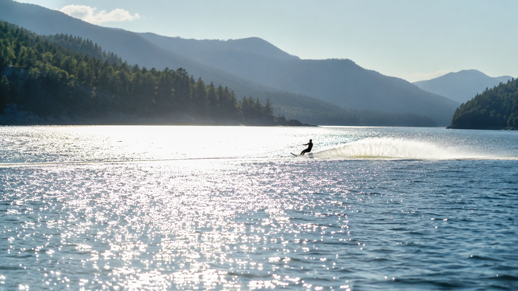 Silhouette lointaine d'un skieur nautique traçant un sillage sur un lac ensoleillé