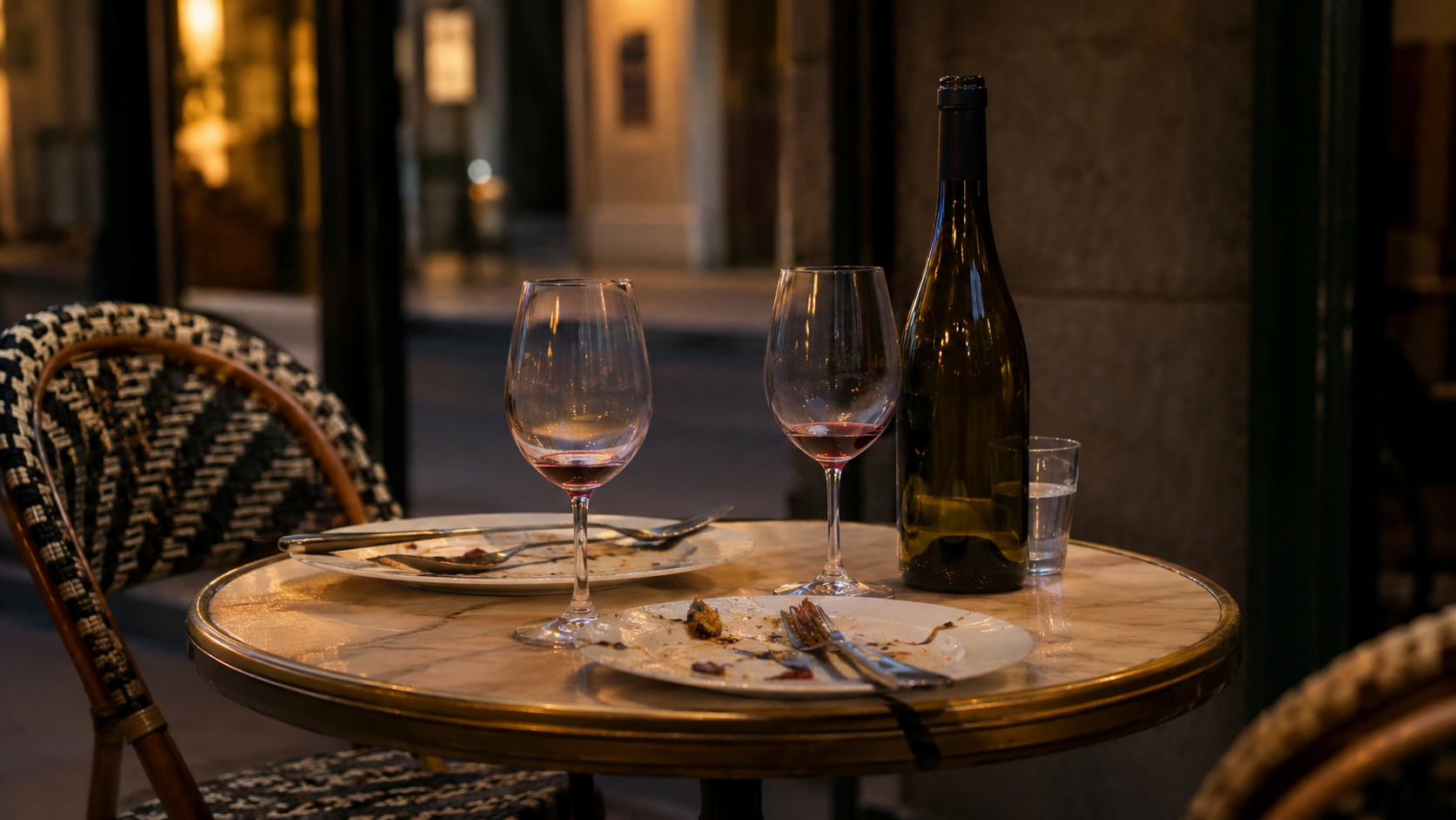 Une table de bistrot français à la tombée du jour après un repas, deux verres de vin et une bouteille presque vide