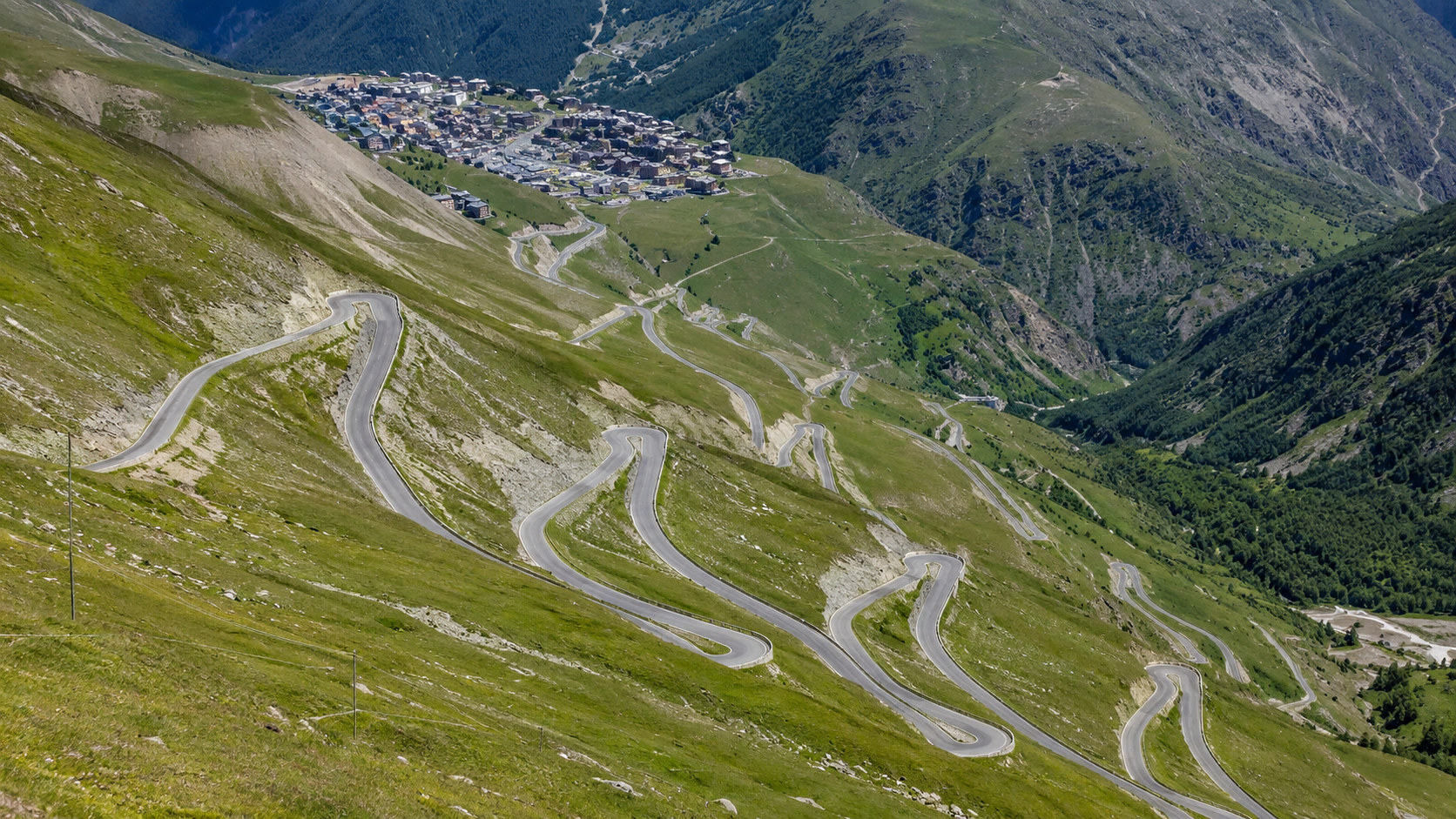 Vue large des lacets d'une ascension alpine célèbre serpentant vers une station de montagne, route vide en été